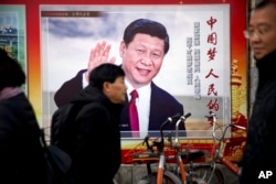 FILE - People walk past a propaganda billboard showing Chinese President Xi Jinping on a street in Beijing, China, March 2, 2018.