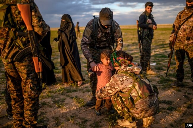 A member of the Kurdish-led Syrian Democratic Forces (SDF) holds a toddler during a security check of her and her mother after they left the IS group's last holdout of Baghuz, in Syria's northern Deir Ezzor province, Feb. 27, 2019.