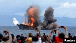 People take pictures of a burning ship as the government destroyed foreign boats that had been caught illegally fishing in Indonesia waters, at Morela village in Ambon island, April 1, 2017.