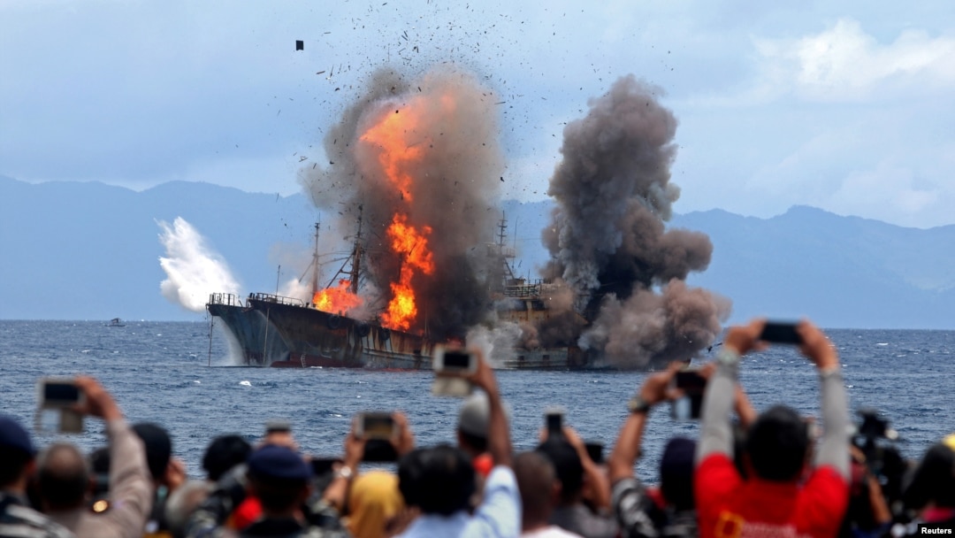 People take pictures of a burning ship as the government destroyed foreign boats that had been caught illegally fishing in Indonesia waters, at Morela village in Ambon island, April 1, 2017.