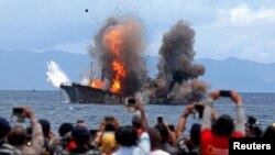 Orang-orang mengambil foto kapal asing yang diledakkan pemerintah setelah tertangkap karena melakukan penangkapan ikan ilegal. Foto diambil di Desa Morela, Ambon, 1 April 2017 (foto: Antara Foto/Izaac Mulyawan via Reuters)