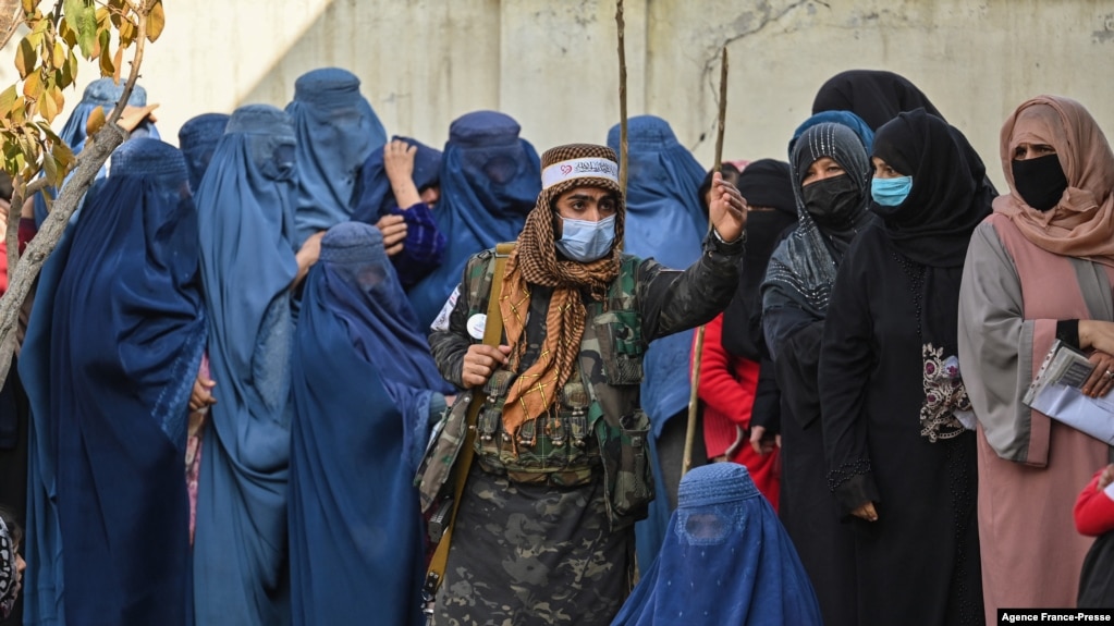 FILE - A Taliban fighter (C) stands guard as women wait in a line during a World Food Program cash distribution in Kabul, Nov. 29, 2021.