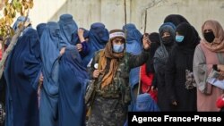 FILE - A Taliban fighter (C) stands guard as women wait in a line during a World Food Program cash distribution in Kabul, Nov. 29, 2021.
