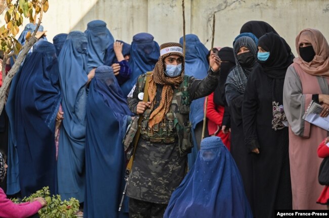 FILE - A Taliban fighter (C) stands guard as women wait in a line during a World Food Program cash distribution in Kabul, Nov. 29, 2021. (Photo by Hector RETAMAL / AFP)