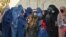 FILE - A Taliban fighter (C) stands guard as women wait in a line during a World Food Program cash distribution in Kabul, Nov. 29, 2021.