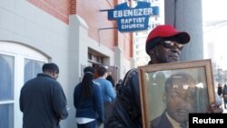 FILE - James Pender, Jr. stands in front of old Ebenezer Baptist Church where slain civil rights leader Martin Luther King, Jr. preached while holding a photograph of King, while visiting the King Center in Atlanta, Jan. 20, 2014.