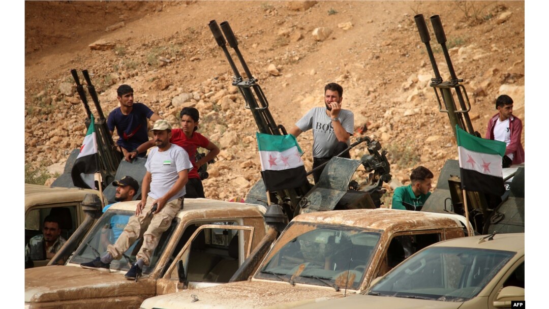 Syrian rebel fighters man anti-aircraft guns mounted in the back of pickup trucks during a military parade near the southern city of Daraa on June 7, 2018.