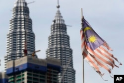 Bendera nasional Malaysia yang tampak lusuh berkibar di depan Menara Petronas di Kuala Lumpur, Malaysia. (Foto: AP)