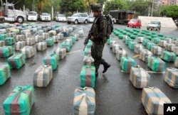 FILE - A police officer guards packages of seized marijuana on display for a media presentation at police headquarters in Cali, Colombia, March 26, 2013. According to police, the 7.7 tons of marijuana were seized from the rebels of the Revolutionary Armed Forces of Colombia, FARC, during a raid in a highway near Cali.