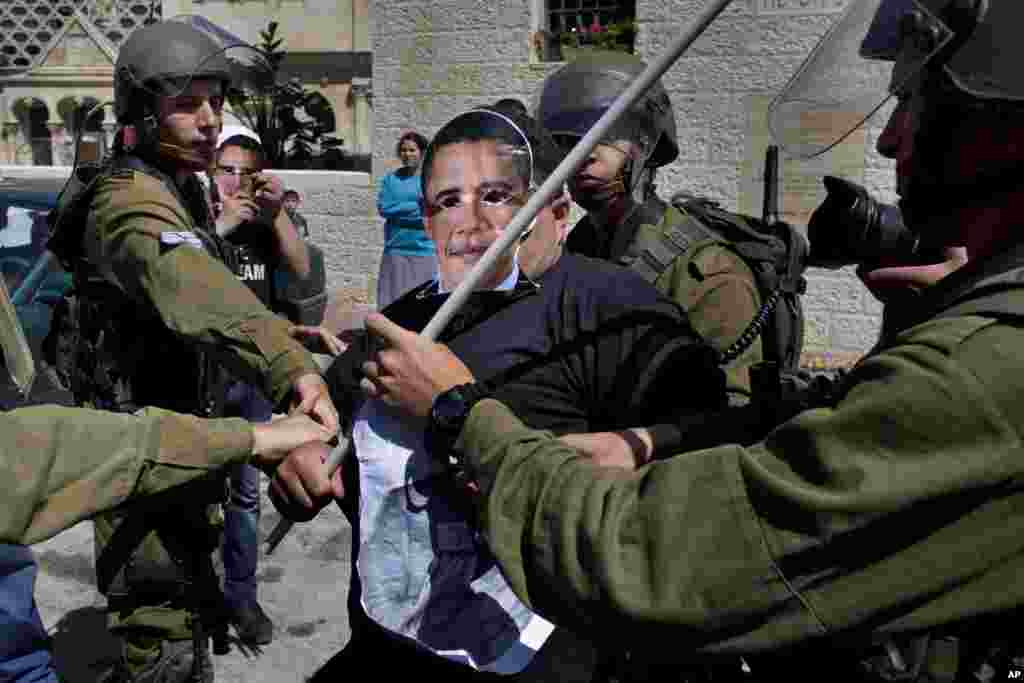 Israeli soldiers scuffle with a Palestinian activist wearing a mask of U.S. President Barack Obama during a protest in the West Bank town of Hebron, March 20, 2013. 