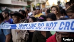 FILE - People stand behind a police line at a crime scene in Tegucigalpa, Honduras, Nov. 19, 2013.