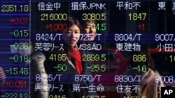 FILE - People are reflected on the electronic board of a securities firm in Tokyo, Japan.