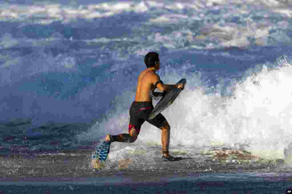 یک موج سوار در حال دوش به سوی موج های ساحل هالیوا ایالت هاوایی امریکا.