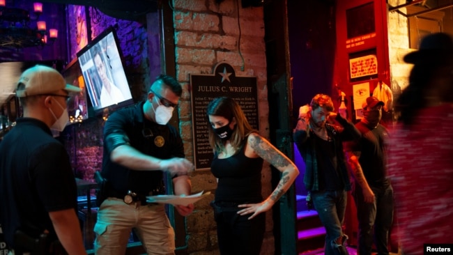 Lindsey Pettita (ketiga dari kiri), manajer bar The Jackalope berbincang dengan petugas pengawas minuman alkohol Texas untuk memeriksa aturan jarak aman untuk meredam penyebaran virus corona (Covid-19), setelah bar buka kembali, di Austin, Texas, 22 Mei 2