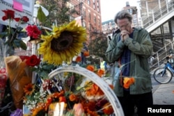 FILE - A man prays after laying flowers at a roadside memorial to the victims of the Oct. 31 attack alongside a bike path at Chambers Street in New York City, Nov. 2, 2017.