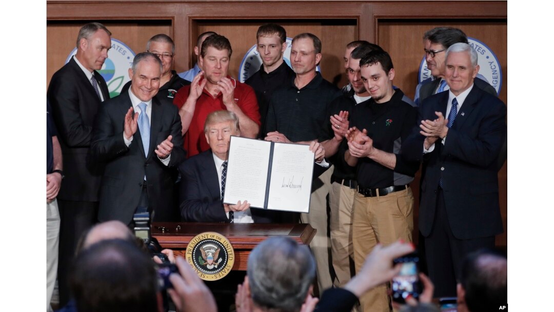 President Donald Trump, accompanied by coal miners and, from left, Interior Secretary Ryan Zinke, EPA Administrator Scott Pruitt, second from right, Energy Secretary Rick Perry, and Vice President Mike Pence, far right, holds up the signed Energy Independence Executive Order, March 28, 2017, at EPA headquarters in Washington.