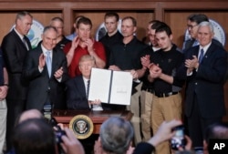 President Donald Trump, accompanied by coal miners and, from left, Interior Secretary Ryan Zinke, EPA Administrator Scott Pruitt, second from right, Energy Secretary Rick Perry, and Vice President Mike Pence, far right, holds up the signed Energy Independence Executive Order, March 28, 2017, at EPA headquarters in Washington.