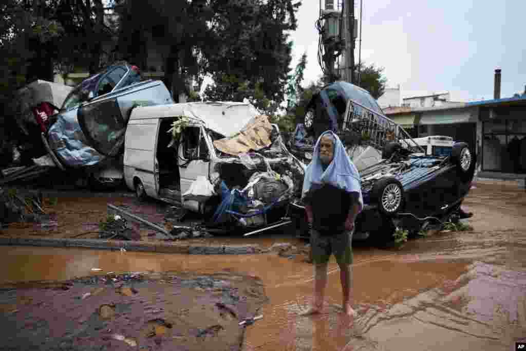 A barefoot man stands in front of a pile of vehicles in the municipality of the Madra area of Athens, Greece. Flash floods in the Greek capital's western outskirts turned roads into torrents of mud and debris, killing at least nine people, inundating homes and businesses, and knocking out a section of a highway.