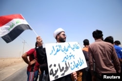 FILE - A protester holds a sign that reads "We ask the decision makers to provide the things we are deprived of" during a protest in south of Basra, Iraq, July 16, 2018.