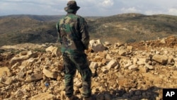 FILE - A Hezbollah fighter looks toward Syria while standing in the fields of the Lebanese border village of Brital, May 9, 2015. 