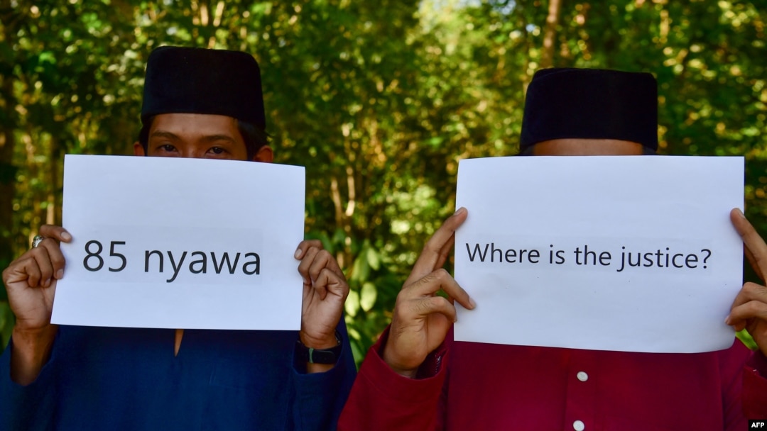 Community members hold up signs in front of a mass grave for victims of the Oct. 25, 2004, Tak Bai Massacre in which 85 Muslims died, most of them by suffocating in Thai army trucks, at a cemetery in Thailand's southern province of Narathiwat on Oct. 25, 2024.