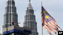 Bendera nasional Malaysia yang terkoyak berkibar di depan Menara Petronas di Kuala Lumpur, Malaysia. Pemerintah Malaysia mengatakan akan menghapus hukuman mati dan menghentikan semua eksekusi. (Foto: AP)