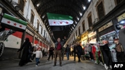 Un hombre reacciona mientras sostiene una bandera de la oposición siria a lo largo de un callejón del mercado cubierto de Hamidiyah en la parte antigua de Damasco, el 10 de diciembre de 2024.