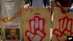 Anti-coup protesters stand behind a line of makeshift shields marked with the three-fingered salute and the defaced image of Commander in chief, Senior Gen. Min Aung Hlaing, as they gather to protest in Yangon, Myanmar, March 9, 2021.