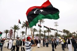 FILE - A Libyan man waves a Libyan flag during a demonstration to demand an end to the Khalifa Haftar's offensive against Tripoli, in Martyrs' Square in central Tripoli, Libya, April 26, 2019.