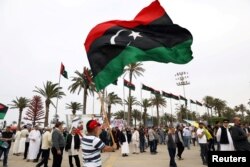 FILE - A Libyan man waves a Libyan flag during a demonstration to demand an end to Khalifa Haftar's offensive against Tripoli, in Martyrs' Square in central Tripoli, Libya, April 26, 2019.