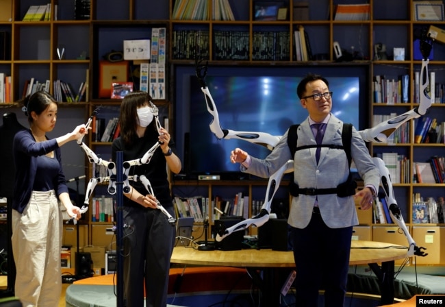 Staff members control the robot arm control unit which is synced with wearable robot arms "Jizai Arms" which Masahiko Inami of the University of Tokyo wears during its demonstration at the school's lab in Tokyo, Japan, June 22, 2023. (REUTERS/Kim Kyung-Hoon)