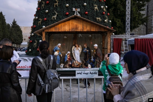 People take pictures of the Christmas tree and nativity scene in Manger Square, outside to the Church of the Nativity, traditionally believed by Christians to be the birthplace of Jesus Christ, ahead of Christmas, in the West Bank city of Bethlehem, Monday, Dec. 5, 2022. (AP Photo/ Mahmoud Illean)