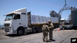 Tentara AS berdiri di samping truk-truk yang membawa bantuan kemanusiaan di dermaga terapung Trident yang dibangun AS sebelum mencapai pantai di pesisir Jalur Gaza, 25 Juni 2024. (Foto: AP)