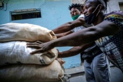 FILE - Workers wearing ill-fitting masks used to curb the spread of the new coronavirus push a cart loaded with sacks in Havana, Cuba, Dec. 23, 2020.