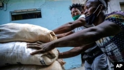 Para pekerja, yang tidak mengenakan masker dengan cara yang tepat, mendorong troli yang dipenuhi karung karung, di Havana, Kuba, pada 23 Desember 2020. (Foto: AP/Ramon Espinosa)