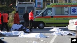 Sheets cover the bodies of cyclists after a speeding car, partially seen at right, plowed head-on into their group in southern Italy on Sunday morning, killing eight of them, in Lamezia Terme, Italy, 05 Dec 2010