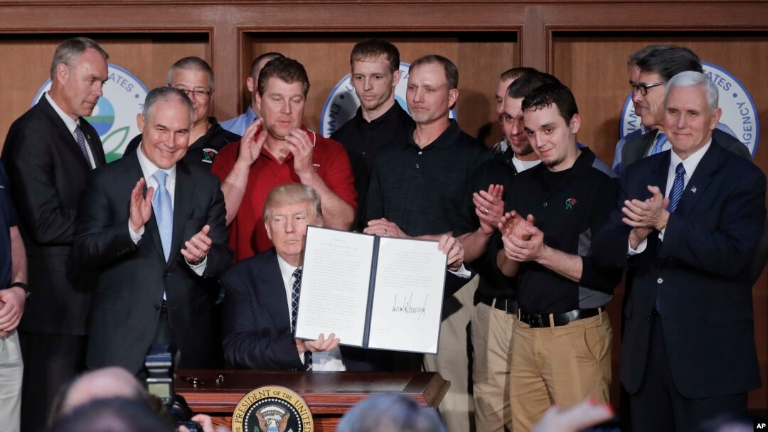 President Donald Trump, accompanied by coal miners and, from left, Interior Secretary Ryan Zinke, EPA Administrator Scott Pruitt, second from right, Energy Secretary Rick Perry, and Vice President Mike Pence, far right, holds up the signed Energy Independence Executive Order, March 28, 2017. 