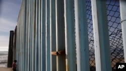 FILE - A woman looks through the border structure separating San Diego, right, from Tijuana, Mexico, Feb. 1, 2017. 