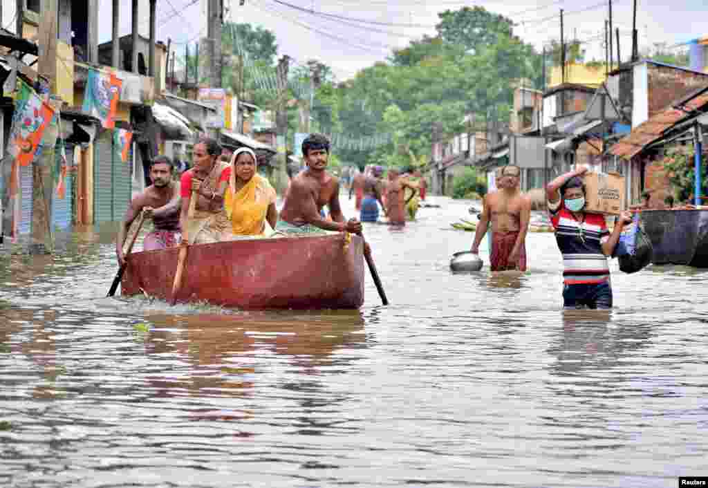 People paddle and wade through a flooded street to collect food and drinking water from a distribution center in Amta town of the Howrah district in the eastern state of West Bengal, India.