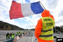 A man with a sign reading "Macron resign" waves a French flag as "yellow vests" (Gilets jaunes) protestors gather to protest against rising oil prices and living costs at the highway's toll of La Barque, Dec. 9, 2018, near Marseille, southern France.