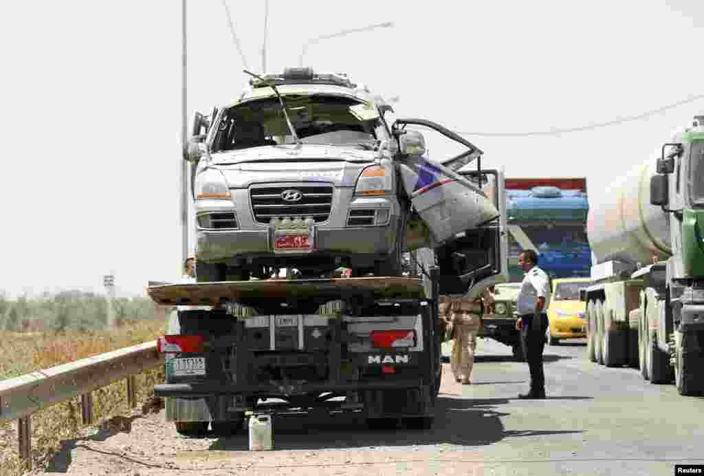 Police prepare to remove a damaged vehicle from the site of a bomb attack in Taji, Iraq, June 17, 2013.