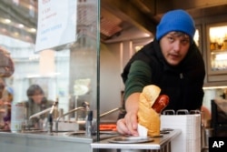 A vendor serves a hot dog at a traditional sausage stand (Wuerstelstand), which are named as intangible cultural heritage by the Austrian UNESCO Commission, in Vienna, Austria, Thursday, Nov. 28, 2024. (AP Photo/Heinz-Peter Bader)