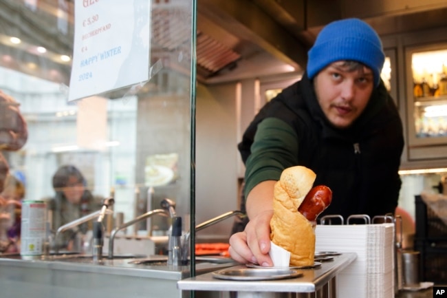 A vendor serves a hot dog at a traditional sausage stand (Wuerstelstand), which are named as intangible cultural heritage by the Austrian UNESCO Commission, in Vienna, Austria, Thursday, Nov. 28, 2024. (AP Photo/Heinz-Peter Bader)