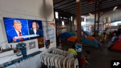 Una migrante camina a una tienda de campaña mientras el debate presidencial entre el candidato republicano Donald Trump, y la candidata demócrata, Kamala Harris, se reproduce en un televisor el martes 10 de septiembre de 2024, en un refugio de migrantes en Tijuana, México.