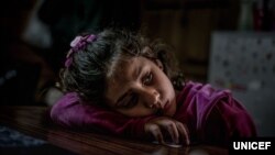 FILE - Mariem, 8, a refugee from Syria, rests in her family’s shelter at a refugee camp in Greece, March 14, 2017. 