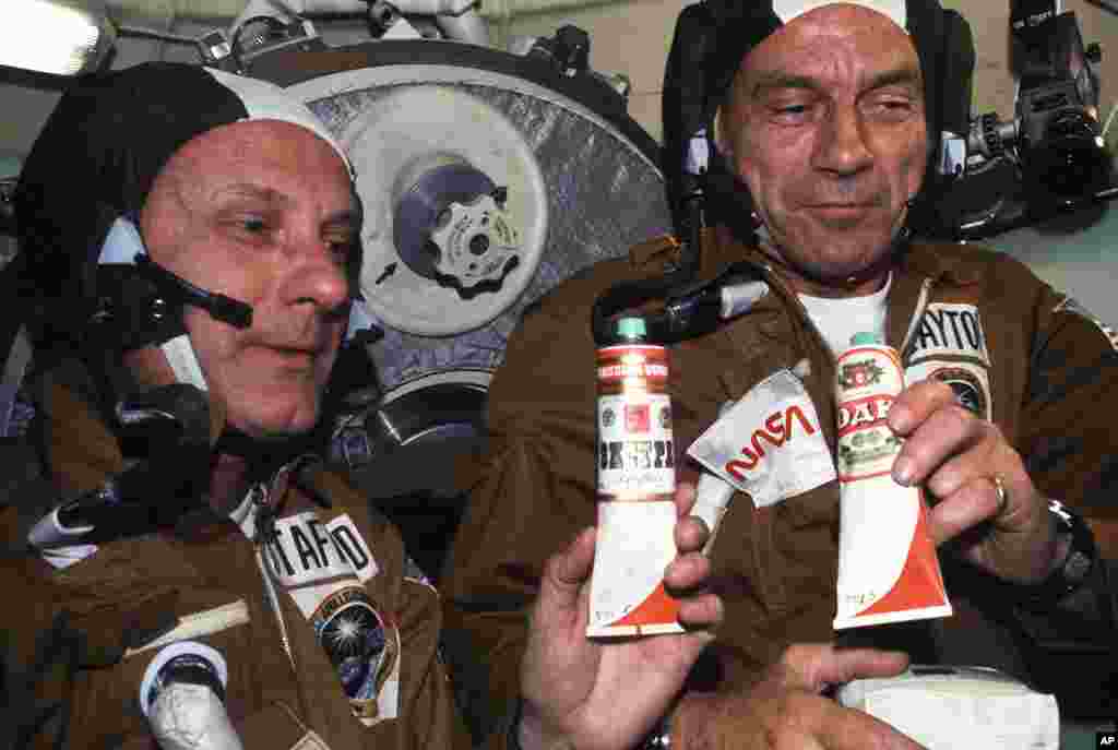 1975: Astronauts Thomas P. Stafford (left) and Donald K. "Deke" Slayton hold containers of Soviet space food in the Soyuz Orbital Module during the joint U.S.-USSR Apollo-Soyuz Test Project docking in Earth orbit mission. The containers hold borsch (beet 