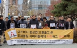 FILE - Victims of Japan's forced labor and their family members arrive at the Supreme Court in Seoul, South Korea, Nov. 29, 2018. The sign reads " Mitsubishi Heavy Industries apologize and compensate victims."