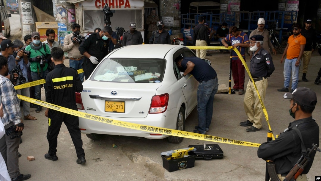 FILE - Investigators examine a damaged car at the site of a shooting incident, in Karachi, Pakistan, July 28, 2021. Gunmen riding on a motorcycle fired into the car that was carrying two Chinese workers.