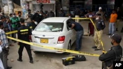 FILE - Investigators examine a damaged car at the site of a shooting incident, in Karachi, Pakistan, July 28, 2021. Gunmen riding on a motorcycle fired into the car that was carrying two Chinese workers.