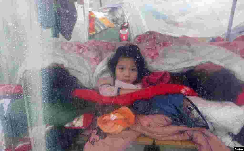 A girl (C) looks out from a makeshift tent during rainy weather as she sleeps with her family after Saturday&#39;s earthquake, in Lingguan town in Baoxing county, Sichuan province, China.